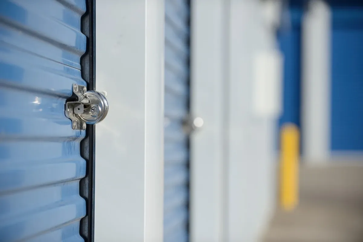 Locked self storage units at a drive-up storage facility with blue doors, white walls, and robust door locks.